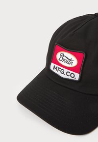 Casquette noire avec un patch cousu rouge et blanc portant l'inscription "Brixtn MFG. CO." en lettres noires. Matériau en coton avec une visière texturée.