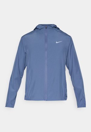 Chaleco deportivo ligero azul con capucha, cremallera completa y un sutil logo de Nike en el lado izquierdo del pecho. Fabricado con una tela suave y transpirable, cuenta con mangas largas.