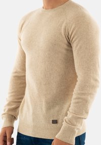 Maglione beige a maglia realizzato in materiale morbido, con scollo rotondo e polsini e orlo a costine, un piccolo dettaglio con logo in basso.