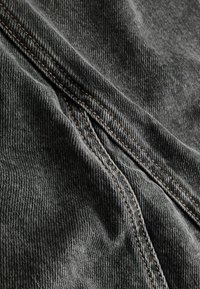 Mørkegrå denimstof med en blød tekstur, prydet med kontrastfarvet orange syninger langs sømmene og synlige skrå folder.
