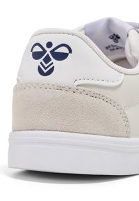 Białe sneakersy z teksturowanym beżowym zamszowym obcasem i granatowym logo. Górna część z gładkiej skóry, biała podeszwa oraz subtelne detale w ściegach.