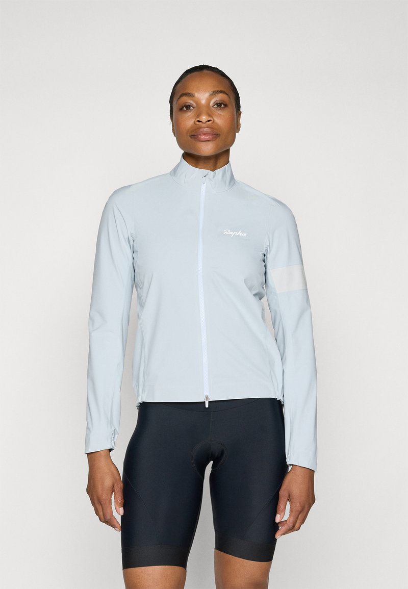 Light blue cycling jacket with a high collar, full-front zipper, and reflective accents. Worn over black cycling shorts. Smooth texture.