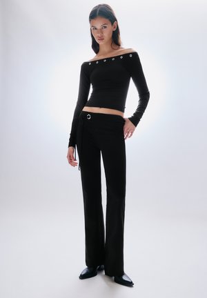 Sort off-the-shoulder top med lange ærmer og sølvbelagte nitter. Kombineret med højttaljede sorte bukser og spidse sorte sko.