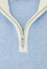 Világoskék kötött pulóver krémszínű cipzáras gallérral. Ezüst cipzárral, texturált fogantyúval és finom, puha fonal textúrával.