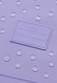 Lila textil táska átlátszó kör alakú díszítésekkel és texturált felülettel. Jellemzője a dombornyomott "JOHNNY URBAN" címke.