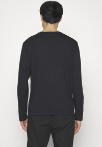 Camiseta de manga larga negra hecha de tela suave. Cuenta con un cuello redondo clásico y un ajuste relajado, con detalles mínimos de costura en el dobladillo.