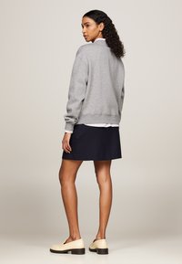 Felpa grigia con polsini a coste, indossata sopra una camicia bianca e blu a righe, abbinata a una gonna blu e mocassini crema.