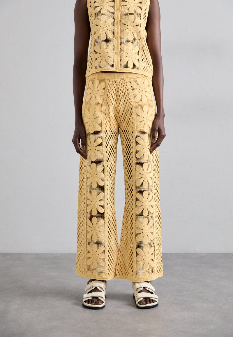 Haut au crochet jaune et pantalon large à motifs floraux ; tissage ouvert texturé ; associé à des sandales blanches à lanières.