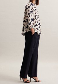 Blusa fluida con un motivo floreale bianco e navy, caratterizzata da maniche a sbuffo. Indossata con pantaloni larghi navy e tacchi neri con cinturini.