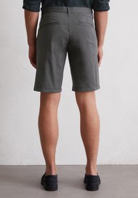 Shorts en coton gris à coupe droite, avec deux poches arrière et un ourlet propre. Le modèle porte des chaussures foncées.