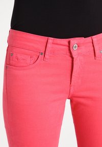 Różowe dżinsy z denimu o wąskim kroju, wyposażone w srebrne zapięcie na guzik, przednie kieszenie oraz haftowane logo na lewej kieszeni.