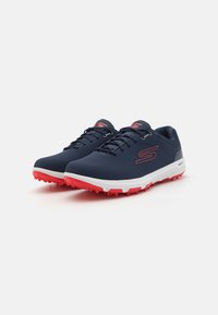 Navy athletic shoes with red accents, textured upper, white midsole, and cleated outsole for traction. Features lace-up design and logo.