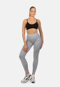 Czarny stanik sportowy w połączeniu z jasnoszarymi legginsami z wysokim stanem, które mają teksturowane akcenty i delikatny wzór, dopełnione białymi sneakersami.