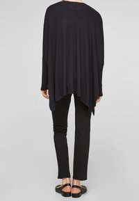 Black loose-fitting sweater with batwing sleeves, high-low hem, and soft texture, paired with black slim pants and black sandals.