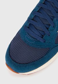 Navy blue sneaker featuring a combination of suede and mesh materials, with textured panels and a rubber sole, highlighting detailed stitching.