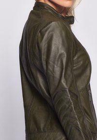 Mörkgrön läderjacka med en figursydd design, ståkrage och detaljerad sömnad. Inkluderar en dragkedjeficka på sidan.