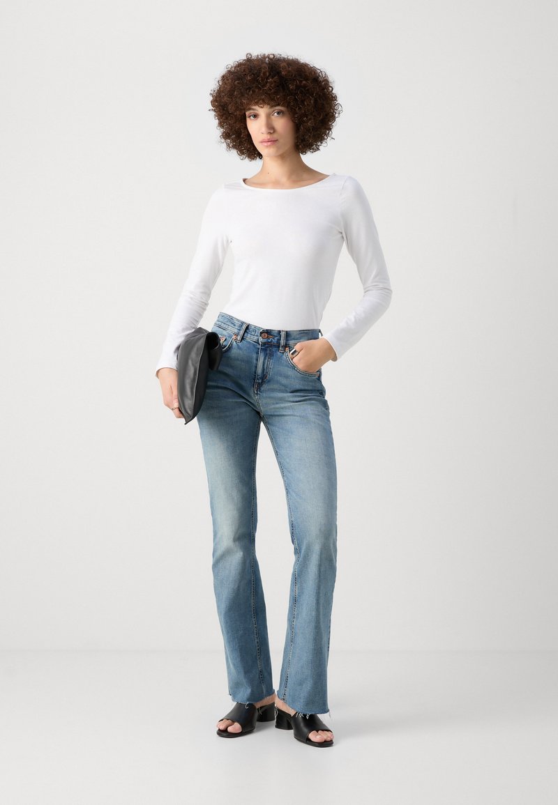 Haut à manches longues blanc, jeans évasés bleu clair, pochette noir, et chaussures noires à bout ouvert. Tissu lisse et design décontracté.