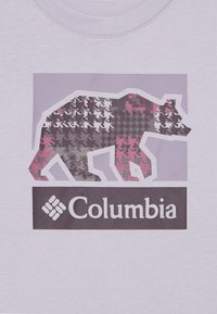 Silvana medvjed sivi, crni i ružičasti šahovski uzorak iznad "Columbia" logotipa na svijetlopurple tkanini.