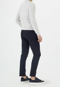 Pull gris clair et pantalon slim bleu marine en coton mélangé, avec une texture douce. Associés à des baskets noires avec semelles blanches.