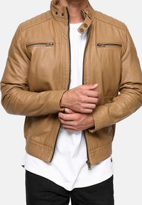 Braune Motorradjacke aus Leder mit hohem Kragen, strukturierten Ärmeln, vorderen Reißverschlüssen und gerippten Akzenten am Saum und den Bündchen. Mit tailliertem Schnitt.