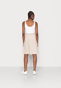 Jupe en lin beige avec une taille élastique, tombant au-dessus du genou. Portée avec un débardeur blanc et des baskets blanches. Design simple et texture naturelle.