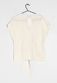 Lekka, kremowa bluzka z pionowymi brązowymi paskami. Luźny krój, okrągły dekolt i ozdobny wiązany detal z tyłu. Miękka w dotyku.
