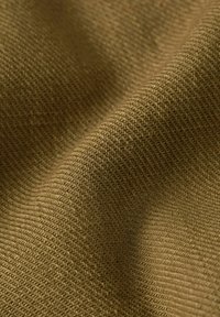 Primo piano di un tessuto verde oliva strutturato, con un motivo intrecciato e pieghe morbide che creano ombre delicate.