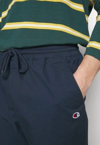 Marinblå joggerbyxor med resårmidja och dragsko, prydda med en liten logotyp på vänster höft, tillverkade av lättviktig tyg.