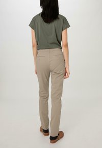 Pantalons slim beige avec deux poches arrière, associés à un haut à manches courtes vert olive, portés avec des chaussures marron sur un fond clair.
