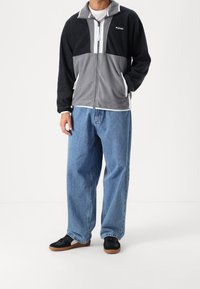 Svart och grå fleecejacka med dragkedja fram, hög krage och fickor. Matchad med lösa blå denimjeans och svarta sneakers med gummisula.