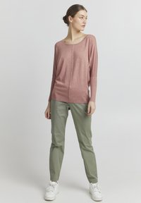 Maglietta a maniche lunghe rosa chiaro in maglia con vestibilità comoda, abbinata a pantaloni aderenti verde oliva e sneakers bianche. Tessuto liscio, design minimale.