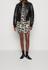 Veste en cuir noir courte sur une robe écrue avec un motif abstrait noir. Des baskets noires avec des semelles blanches complètent la tenue.