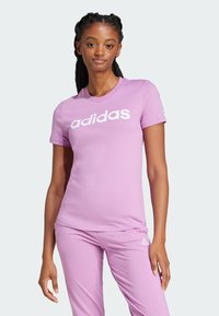 Jasnoróżowy bawełniany t-shirt z krótkimi rękawami i okrągłym dekoltem. Na przodzie znajduje się wyraźne, białe logo „adidas”.