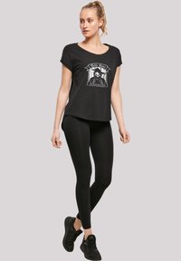 Svart t-skjorte med grafisk trykk som viser et hodeskalle og tekst, parret med svarte leggings og svarte joggesko. Myk, avslappet passform.