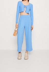 Jasnoniebieski prążkowany crop top z wiązaniem z przodu, zestawiony z luźnymi jasnoniebieskimi spodniami. Beżowe/platformowe buty oraz mała torebka w odcieniu tan.