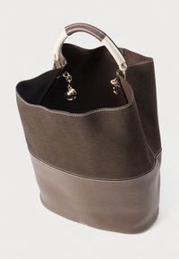 Sac fourre-tout marron avec un dessus en suédine et un bas en cuir lisse, muni d'une poignée de couleur claire contrastante et d'accents en métal doré.