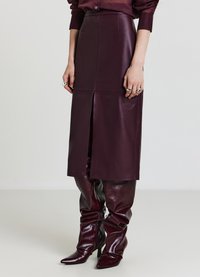 Jupe en cuir bordeaux avec une fente frontale, taille haute et texture lisse, assortie à des bottes bordeaux hautes jusqu'aux cuisses, brillantes et à bouts pointus.