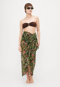 Brun bandeau-top med et midtpunkt, sammen med en grønn, floralmønstret omslagskjørt laget av lett materiale, som avslører bare føtter.
