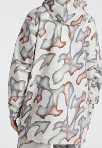 Weiße Kapuzenjacke mit abstraktem Tarnmuster in Grautönen, Braun und Grün, mit elastischen Bündchen und lockerer Passform.