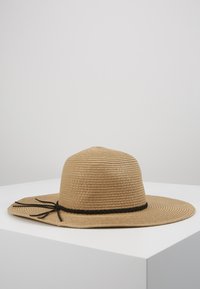 Hut mit breiter Krempe aus Stroh in Beige, mit einem geflochtenen schwarzen Band und gebundenen Akzenten. Strukturierter, texturierter Entwurf mit einer informellen Form.