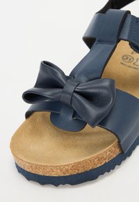 Mørkeblå lædersandal med sløjfedetalje, kork-fodsål og teksturert gummisåle. Åpen design med justerbar stropp.