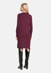 Bordowa sukienka do kolan z długimi rękawami, teksturowaną tkaniną i zaokrąglonym kołnierzykiem, w połączeniu z błyszczącymi czarnymi kozaczkami za kolano.