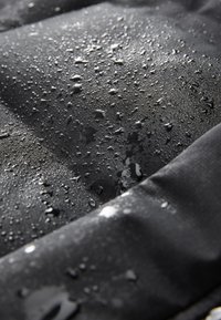 Tissu imperméable noir à surface texturée, présentant des gouttelettes d'eau qui s'accumulent sur le matériau, mettant en évidence ses propriétés hydrofuges.