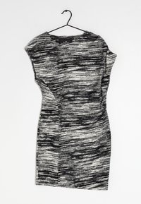 Schwarz-weißes Kleid, das an einem Haken hängt, mit einem strukturierten, abstrakten Muster, kurzen Ärmeln und einer taillierten Form.