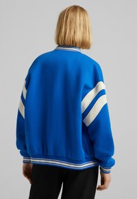 Niebieska bluza z białymi paskami, ściągaczami przy rękawach i u dołu, oraz luźnym krojem. Gładka tekstura i okrągły dekolt.
