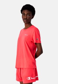 Rød bomulds T-shirt med korte ærmer og lille logo, parret med matchende shorts med et større logo. Enkel, afslappet design.
