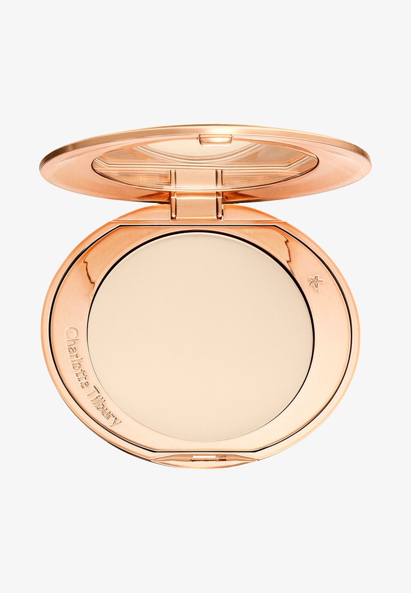 Poudre compacte dans un boîtier rond en or rose avec un couvercle à charnière et un miroir, étiqueté Charlotte Tilbury sur le bord.