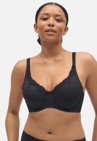 Sostén negro de tela texturizada con encaje, que presenta tirantes ajustables y soporte de aros. Forma suave y diseño sin costuras.