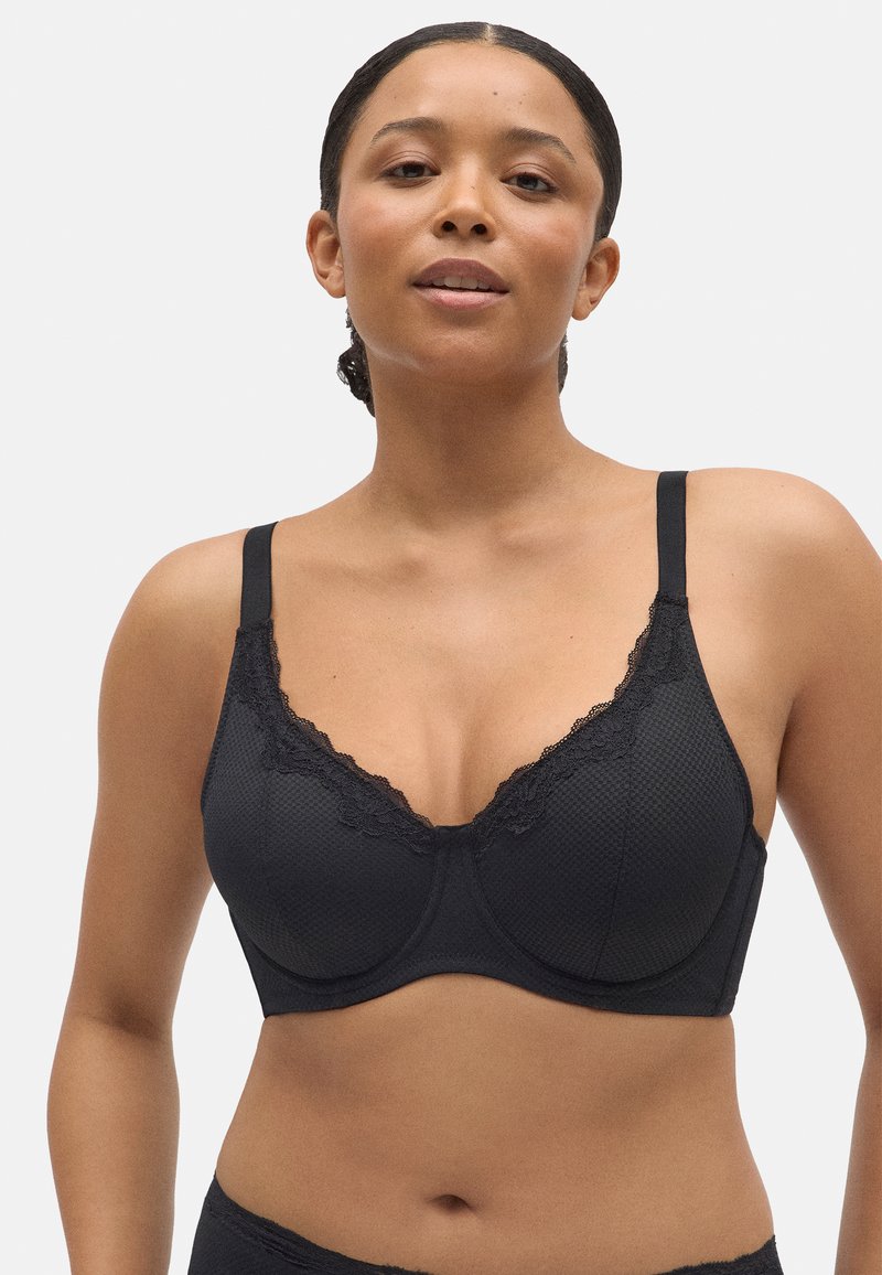 Sostén negro de tela texturizada con encaje, que presenta tirantes ajustables y soporte de aros. Forma suave y diseño sin costuras.