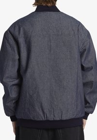 Denim bomberjacka i mörkblått med en ribbad marinblå krage och muddar, med en avslappnad passform och elastisk nederkant. Bakifrån visad.